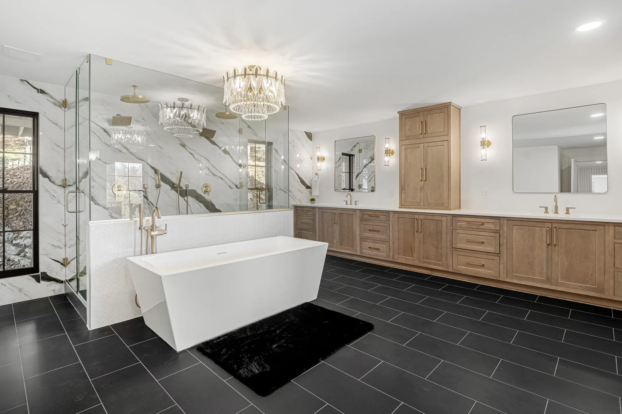 Remodeled primary bathroom with a freestanding tub, slate-look tile floor, wood double vanity and a chandelier