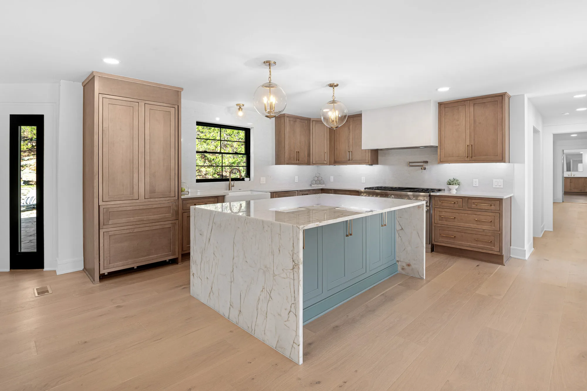 Remodeled kitchen with light oak cabinetry, a marble waterfall island and hardwood floors